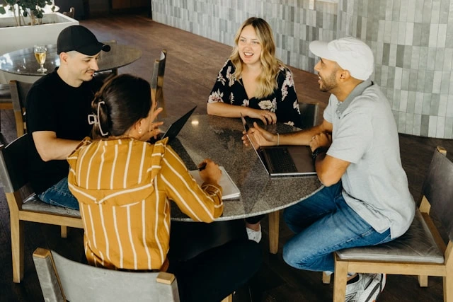 Four diverse professionals collaborating around a table with laptops and a notebook, engaged in a lively discussion about sales strategy and appointment generation.