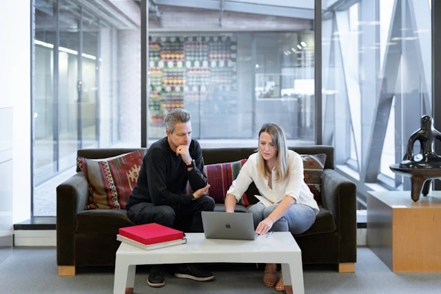 Two business professionals seated on a sofa, intently discussing information on a laptop in a modern office lounge, symbolizing collaboration and strategic planning for appointment generation.